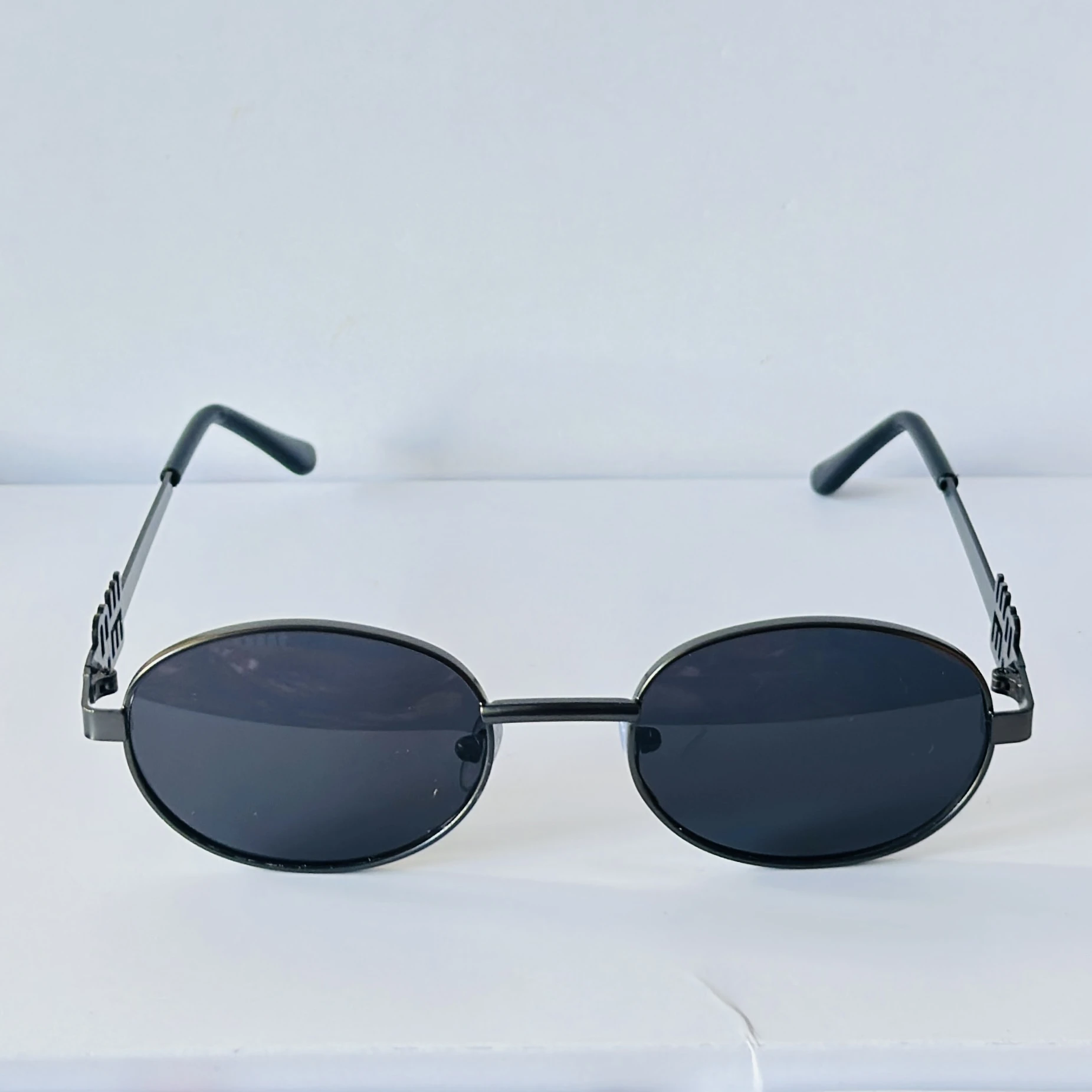sunglasses featuring a distinct black oval frame and small logo detailing on the lenses