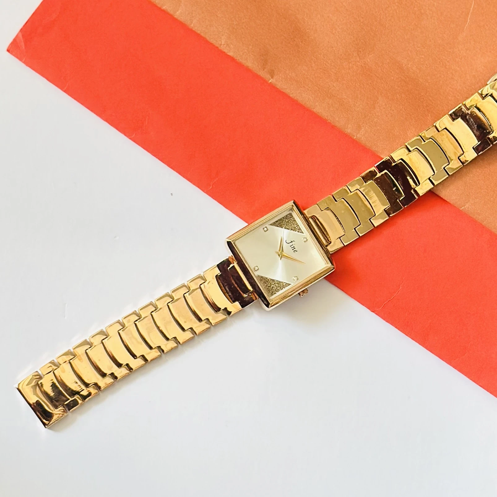Gold -tone analog watch with a square dial and a metal strap.