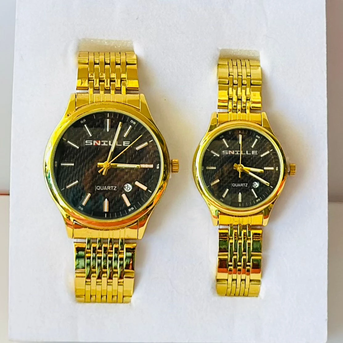 pair of Snille Date Series analog quartz watches for men and women with gold-tone link bracelets and black dials.