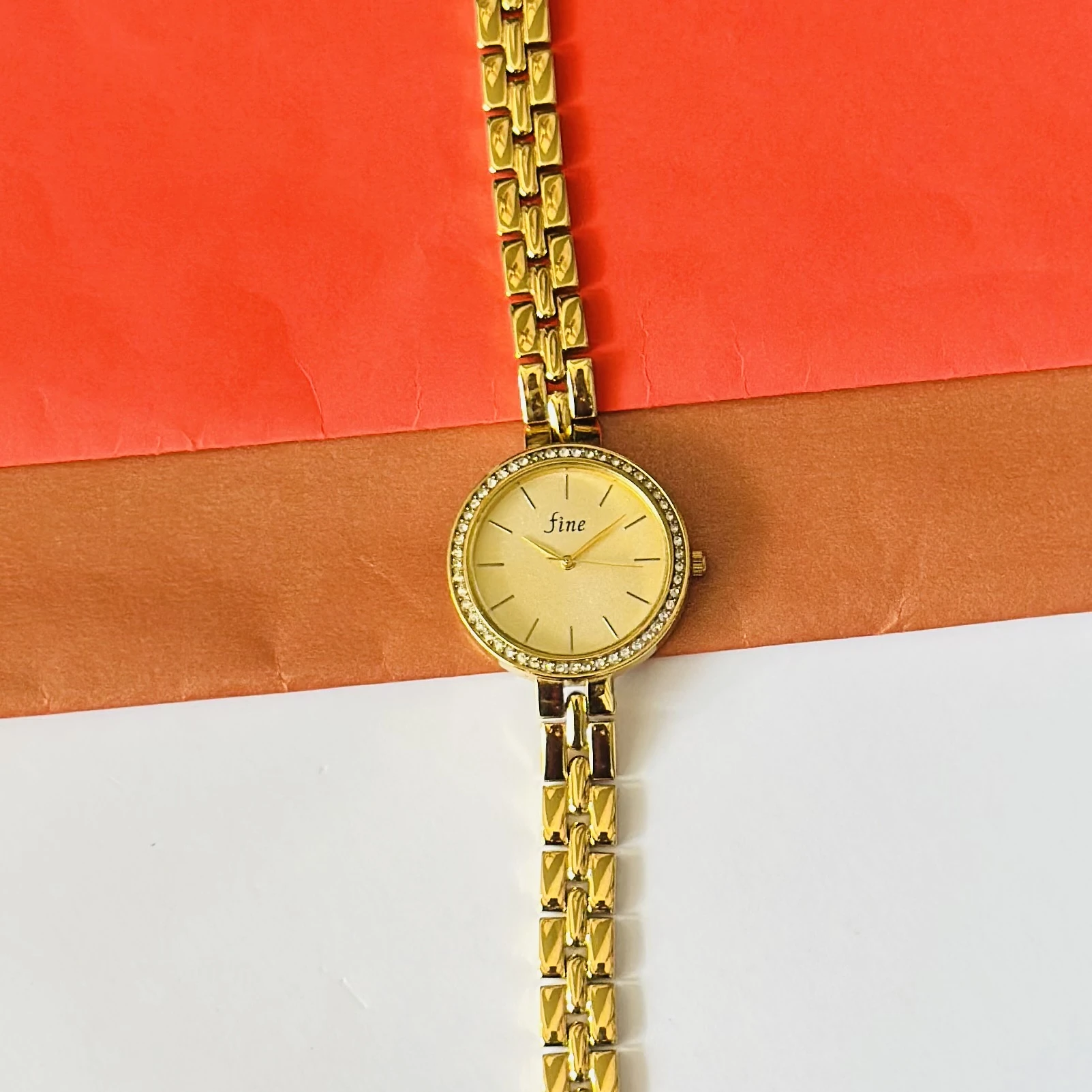 Gold tone women's analog wrist watch with a crystal-encrusted bezel and a metal link strap.