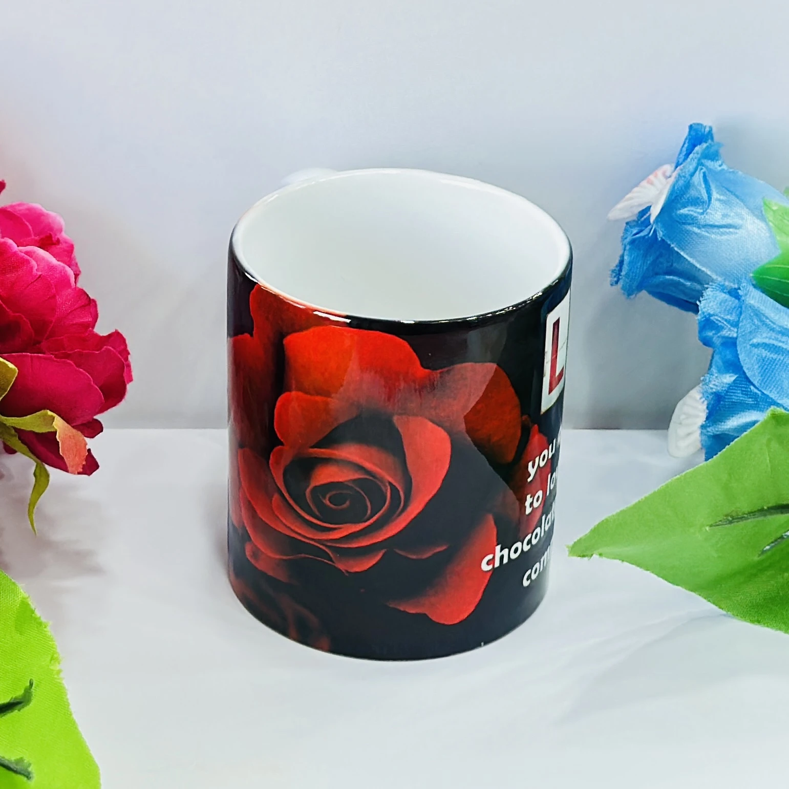 Black ceramic coffee mug with a red rose design.……33J49Y