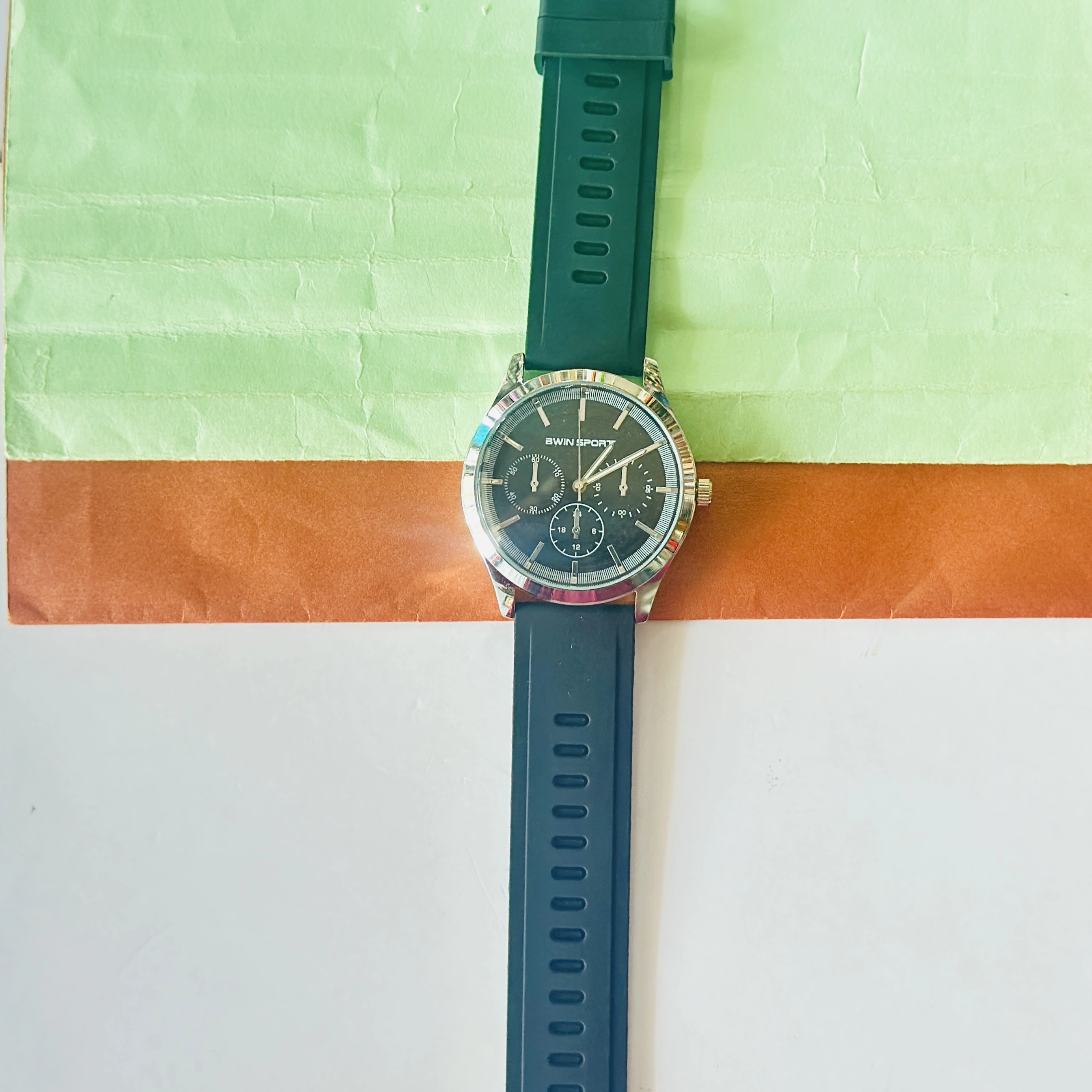 watch features a black dial with sub-dials and a green silicone strap.
