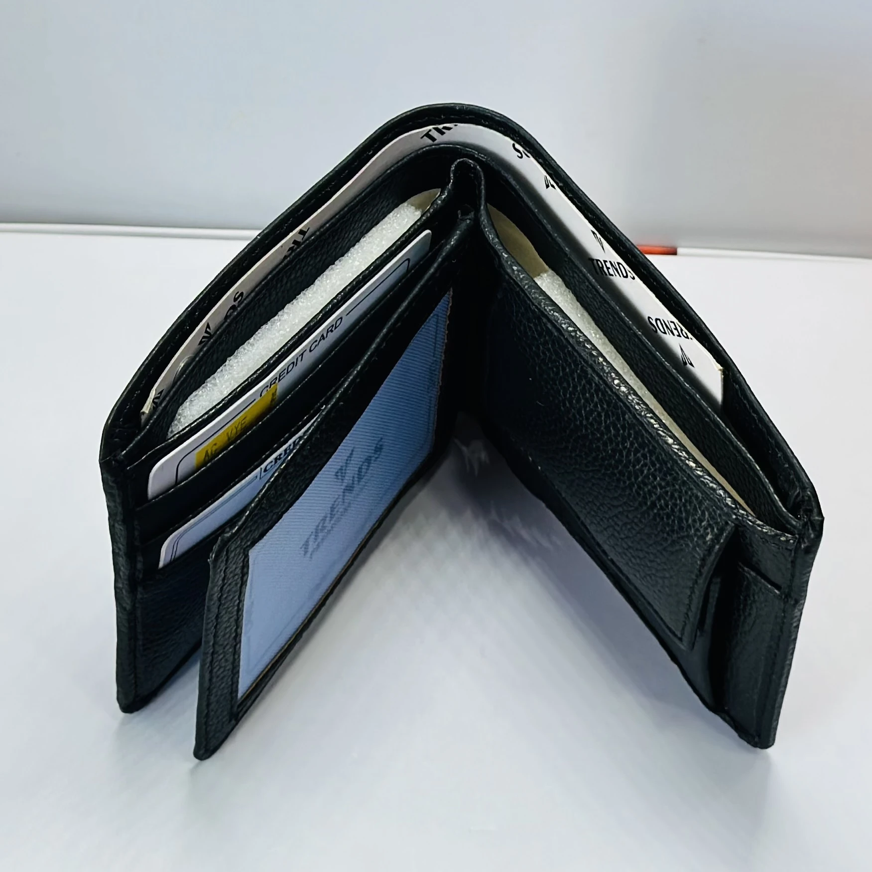 Black leather bifold wallet with a "Trends" logo.