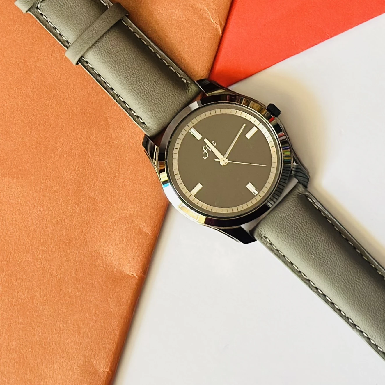 watch with a gray leather strap and a black dial.