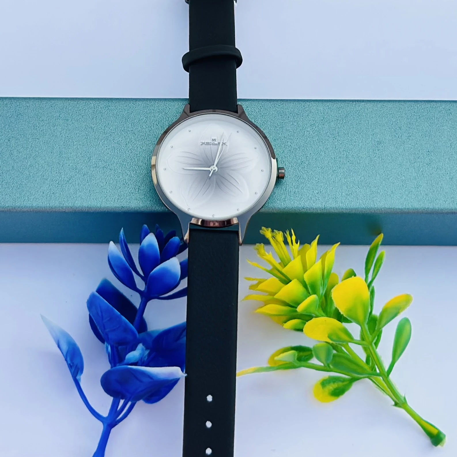 women's analog watch with a silver round dial featuring a white and grey floral pattern and a black leather strap.