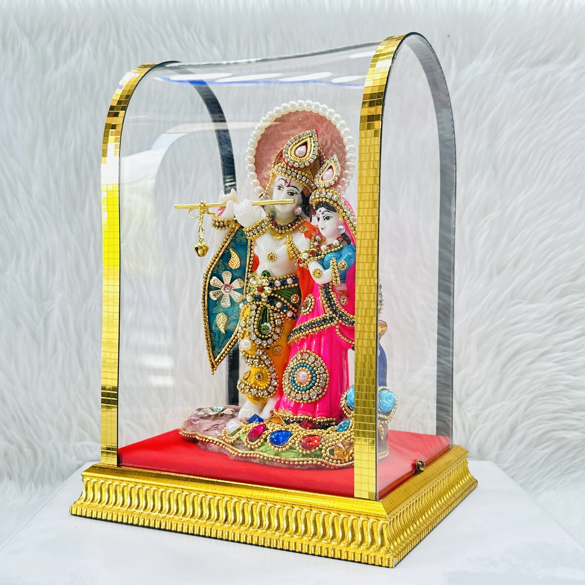 Decorative Radha Krishna statue enclosed in a protective glass dome.