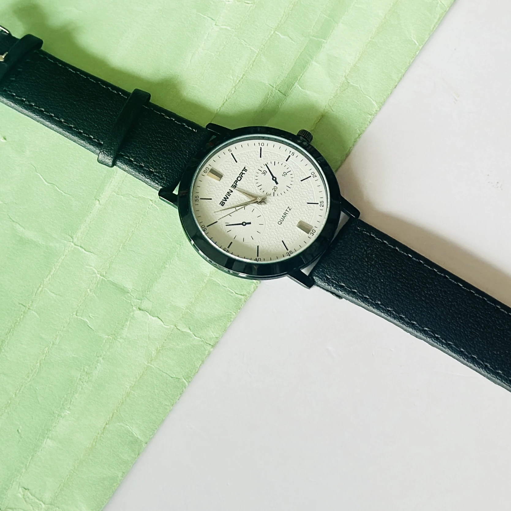 Quartz’s wristwatch featuring a white dial, black markers, and a matching black leather strap.