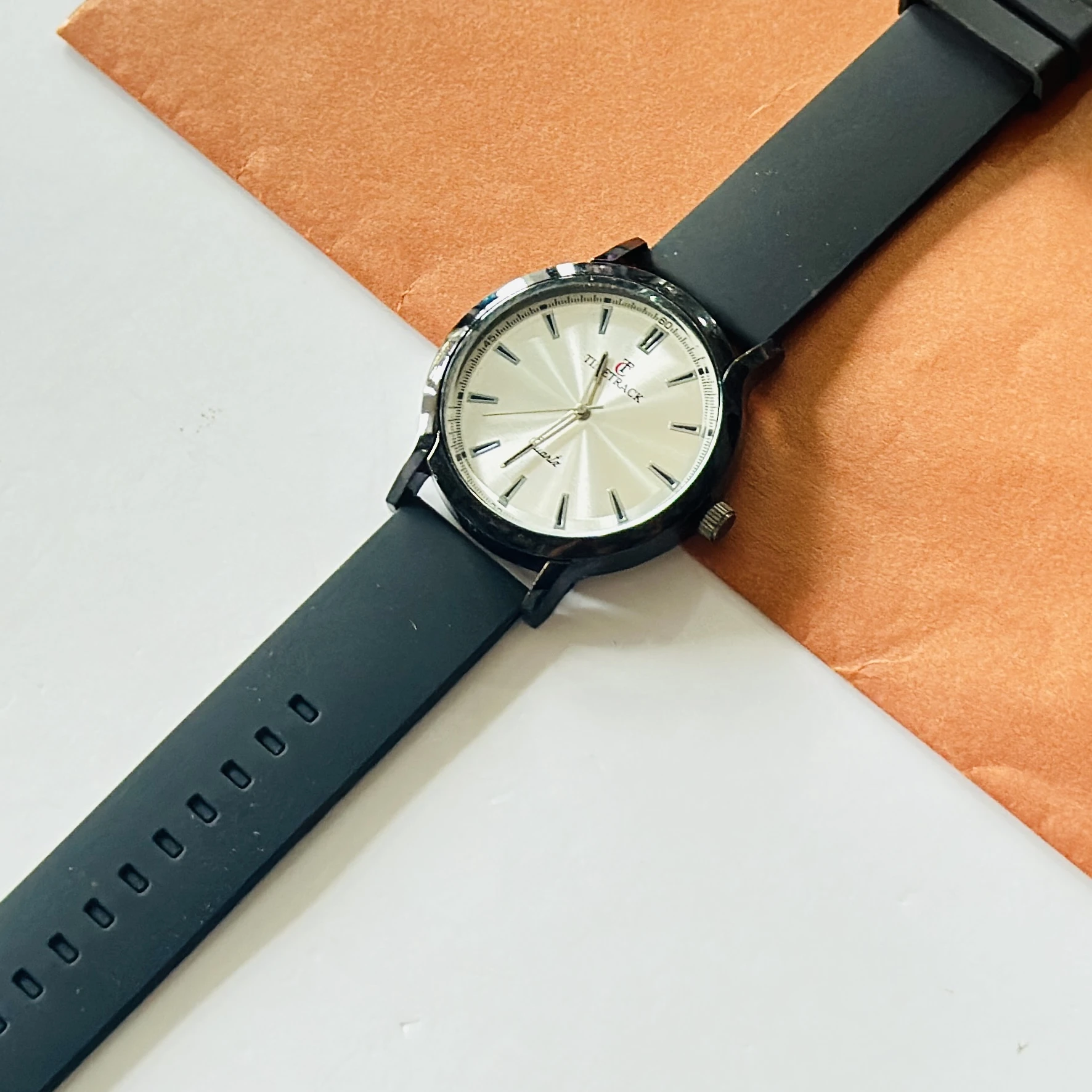 Timitrack brand quartz analog wristwatch with a silver-toned dial and a black silicone strap.