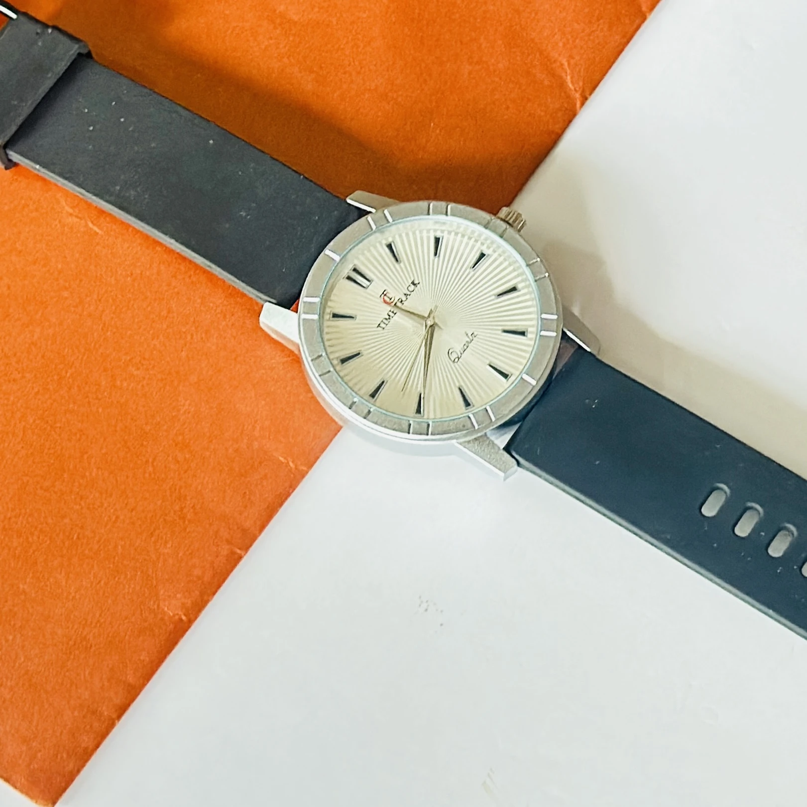 Timitrack brand quartz analog wristwatch with a silver-toned dial and a black silicone strap.